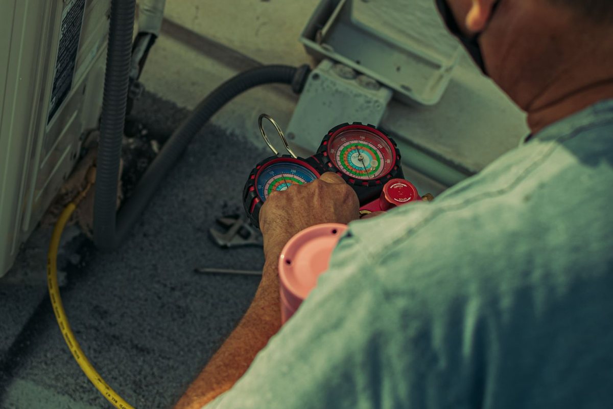 HVAC technician checking refrigerant on an outdoor AC condenser with gauges