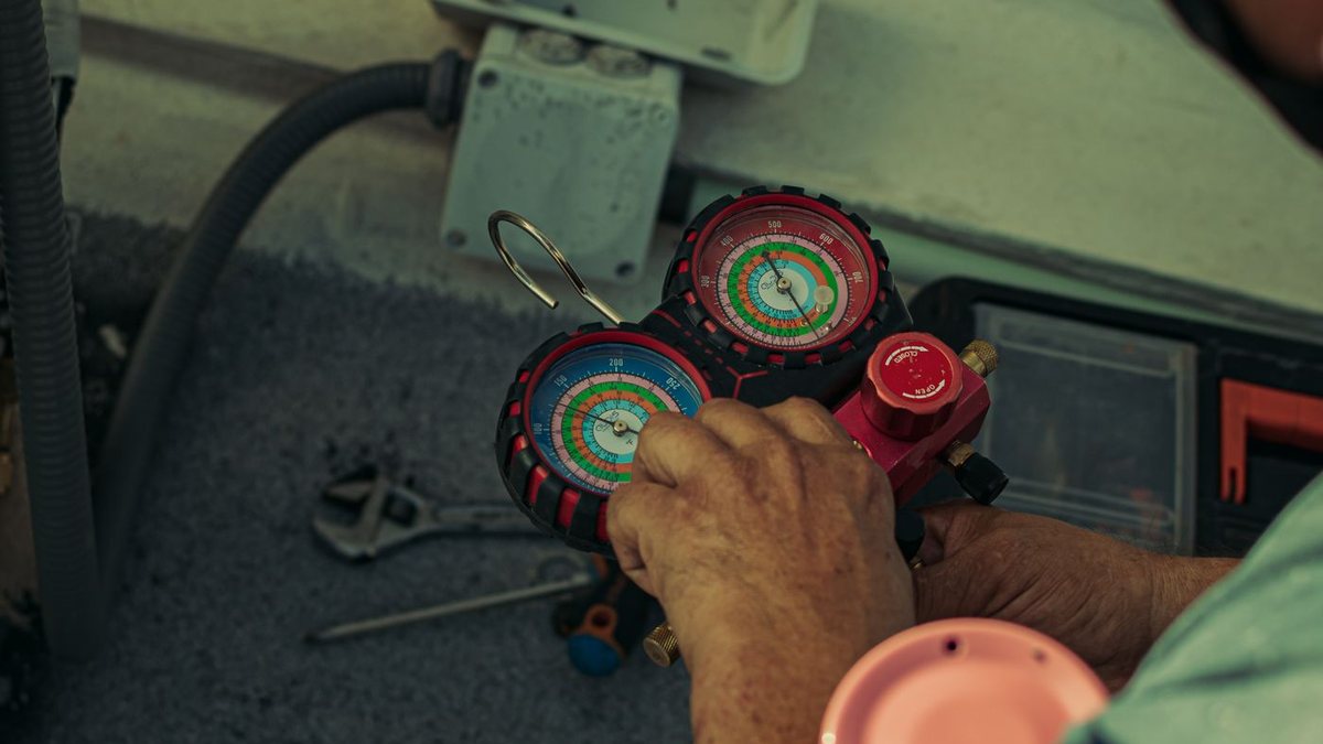 Technician using refrigerant manifold gauges on an air conditioner during a tune-up