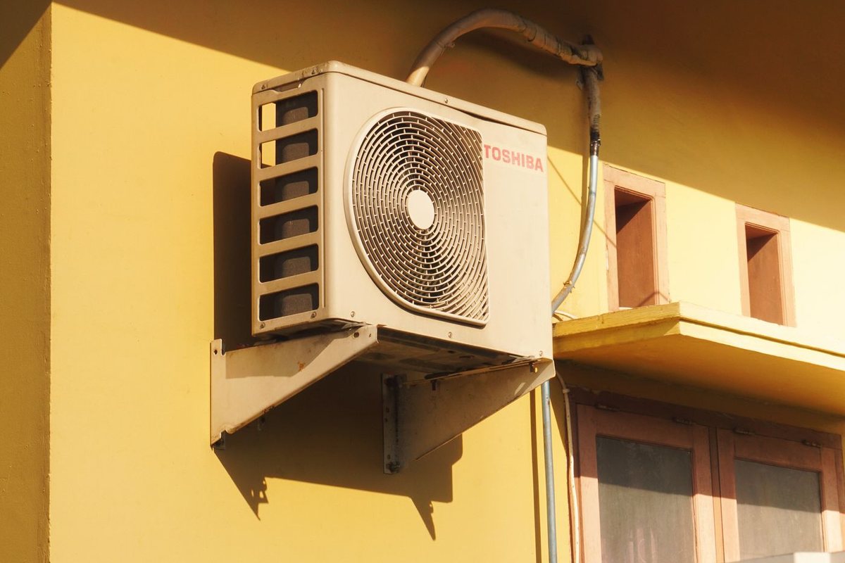 Outdoor air conditioner condenser unit on a home exterior in summer sun
