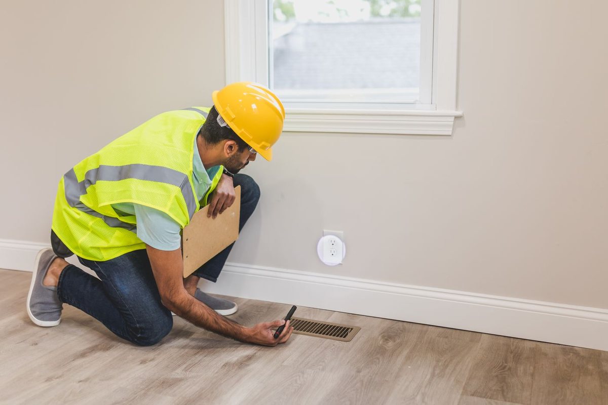 HVAC technician inspecting a home floor air vent register